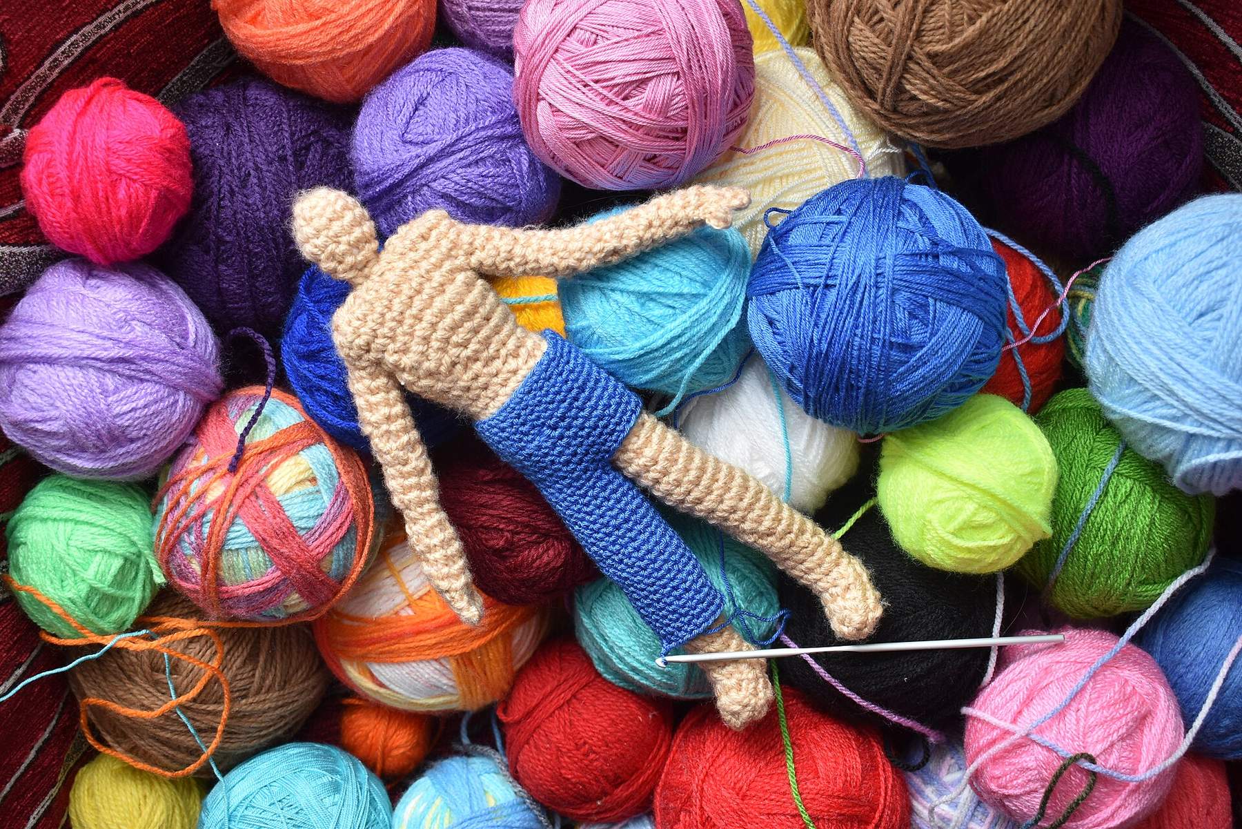 A crocheted doll lying on colourful balls of yarn