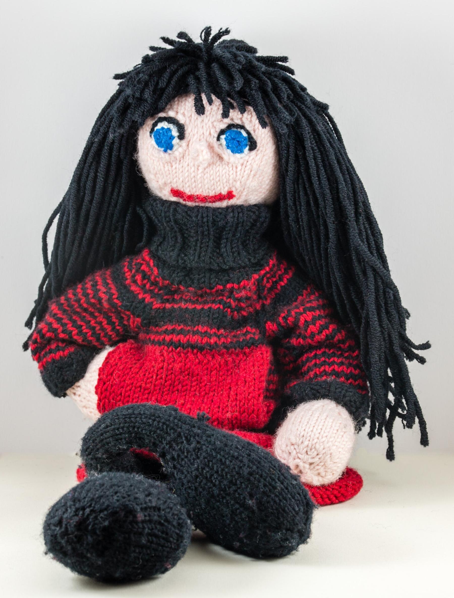 A knitted doll with long black yarn hair and a striped sweater