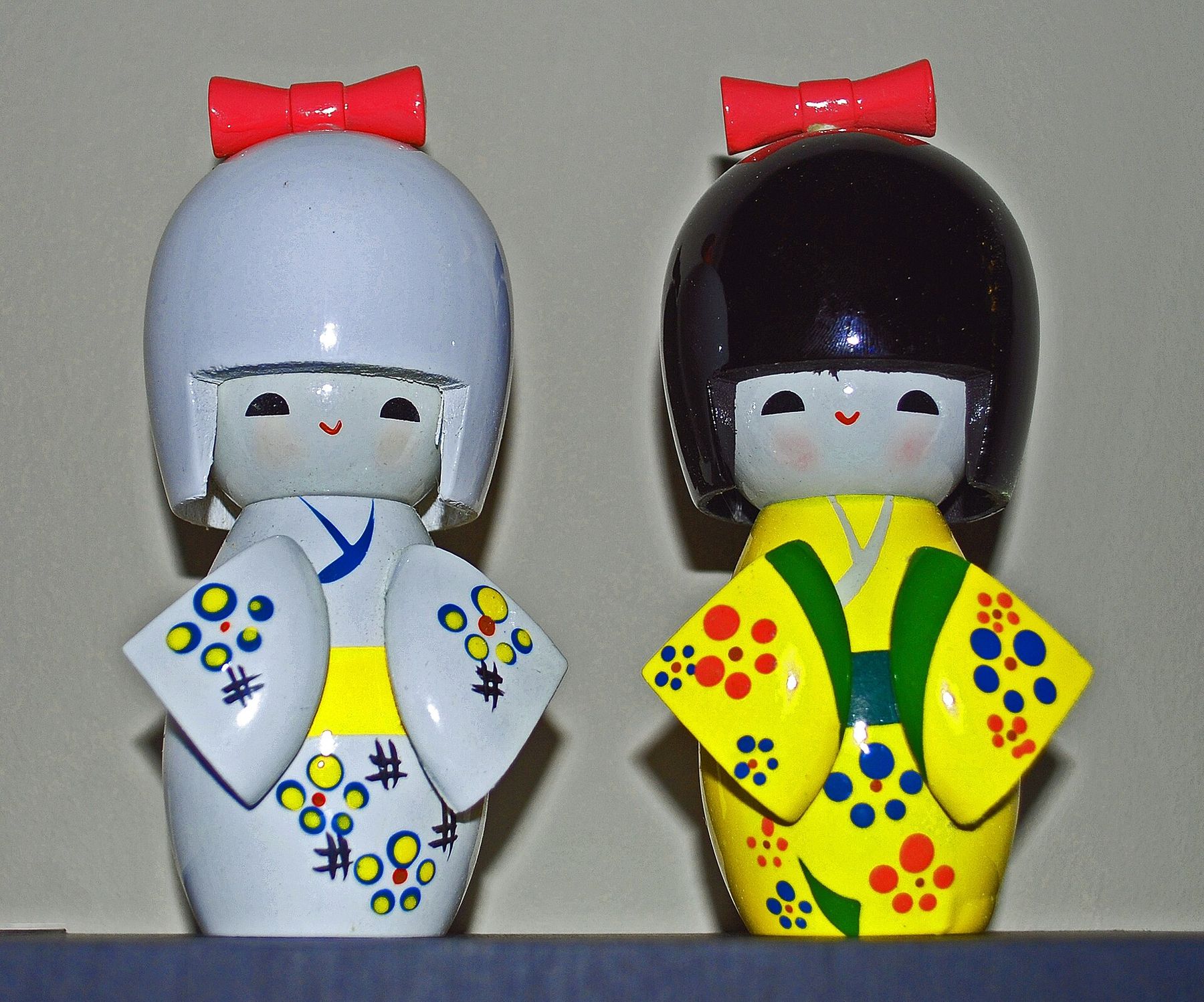 Two glossy doll figurines with red bows and patterned robes