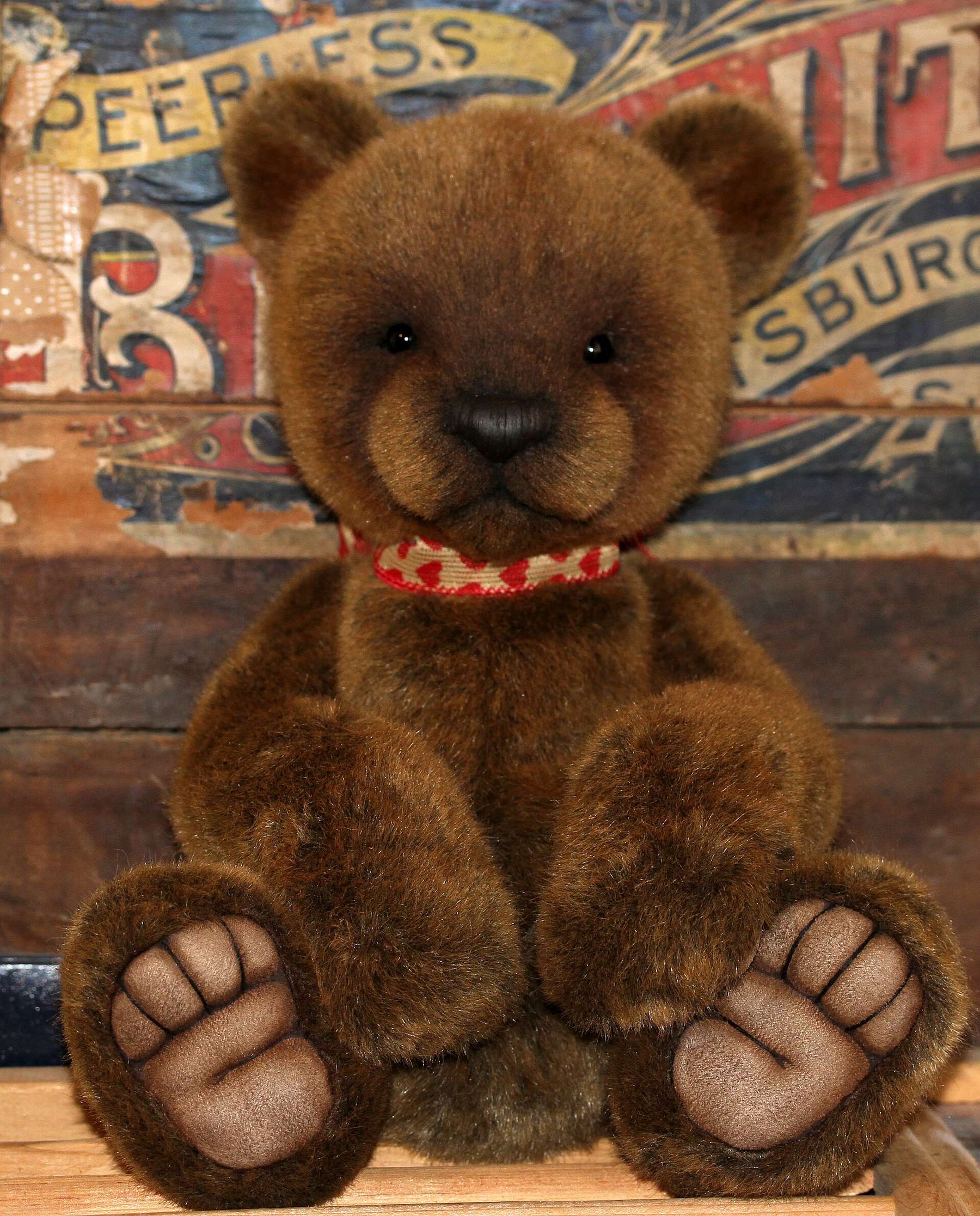 A dark brown teddy bear sitting in front of a vintage painted sign