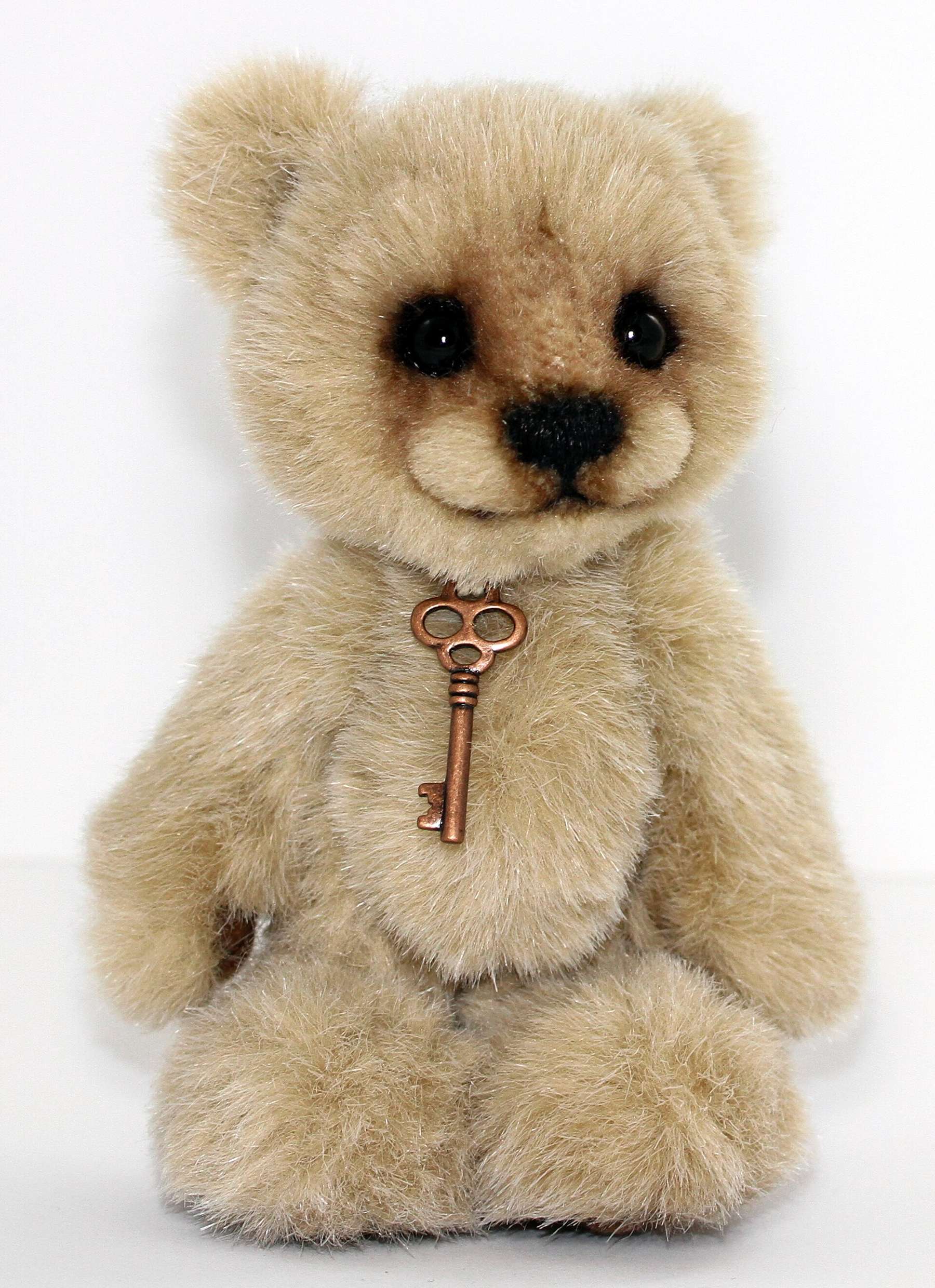 A handmade artist teddy bear wearing a small key pendant