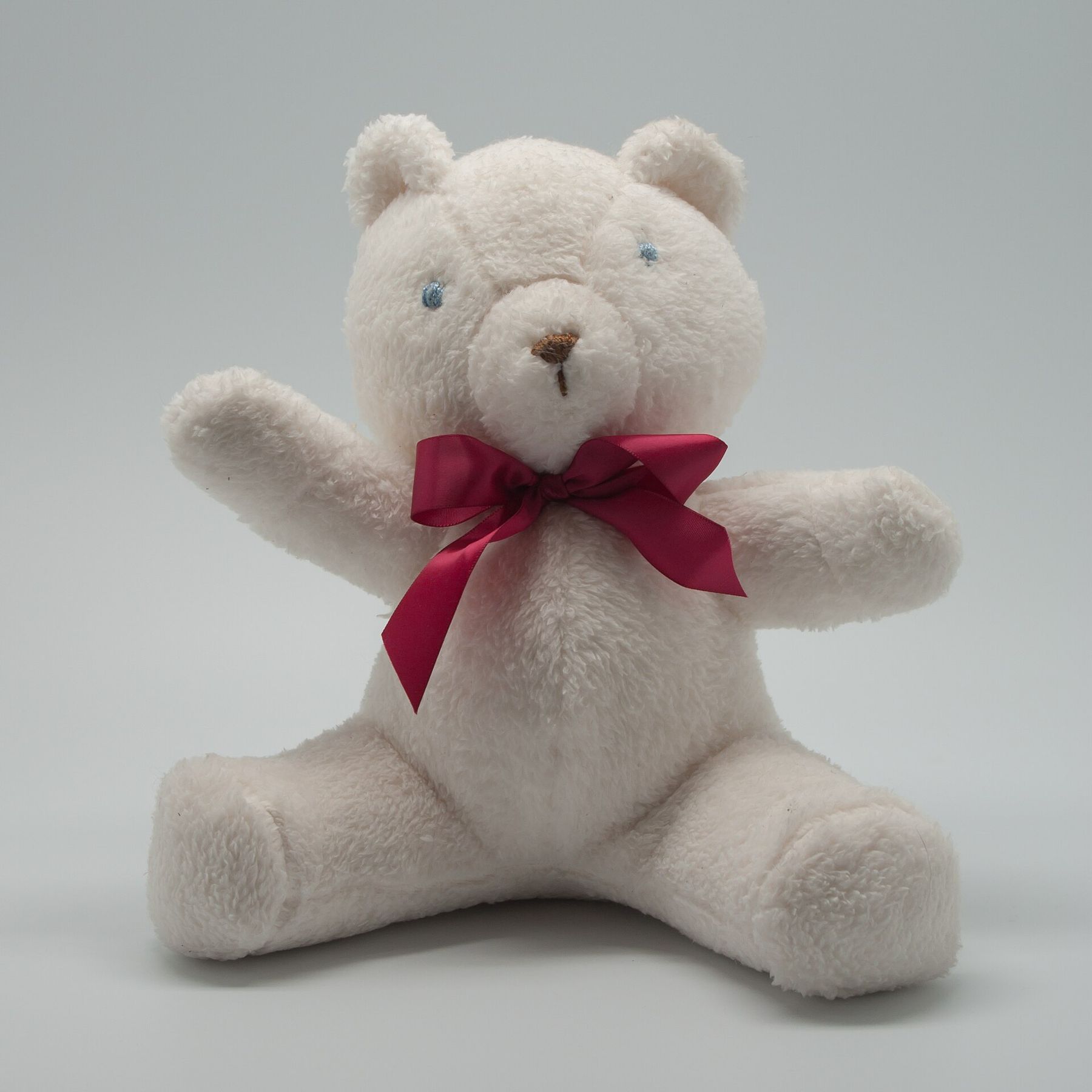 A clean white teddy bear with a red bow